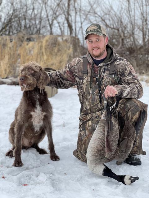 Dave kneeling in snow with his dog and a Canada goose