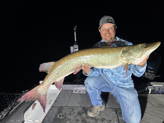 Dave holding a big musky on a boat at night